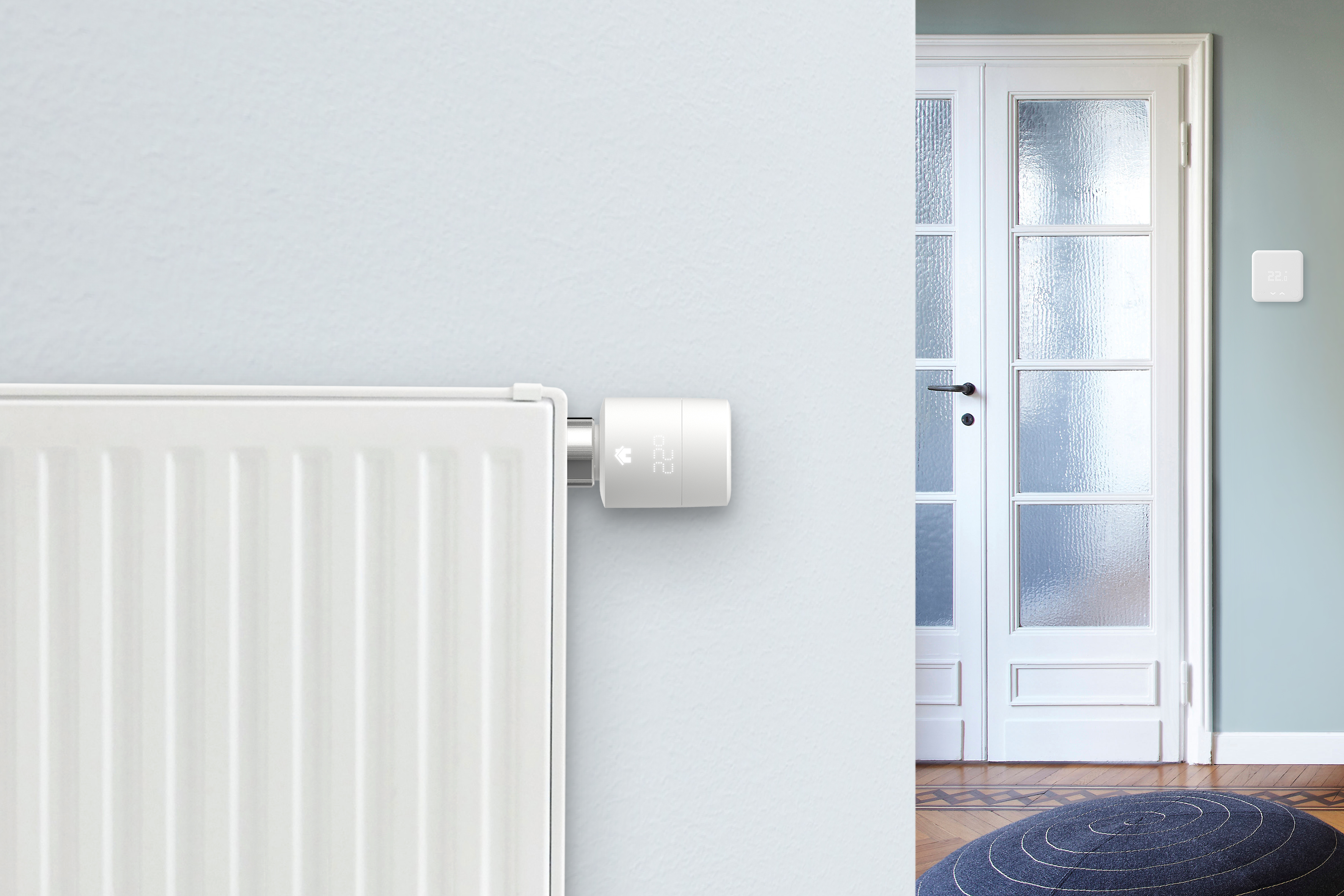 Slimme thermostaat aan de muur, met temperatuurweergave, met een witte deur op de achtergrond.