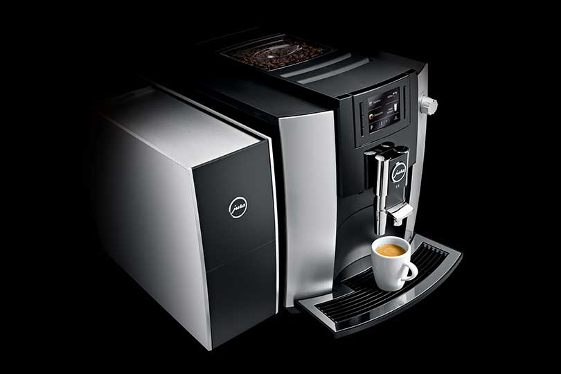 Eine schwarze und silberne Jura Kaffeemaschine mit einer Tasse Kaffee vorne.