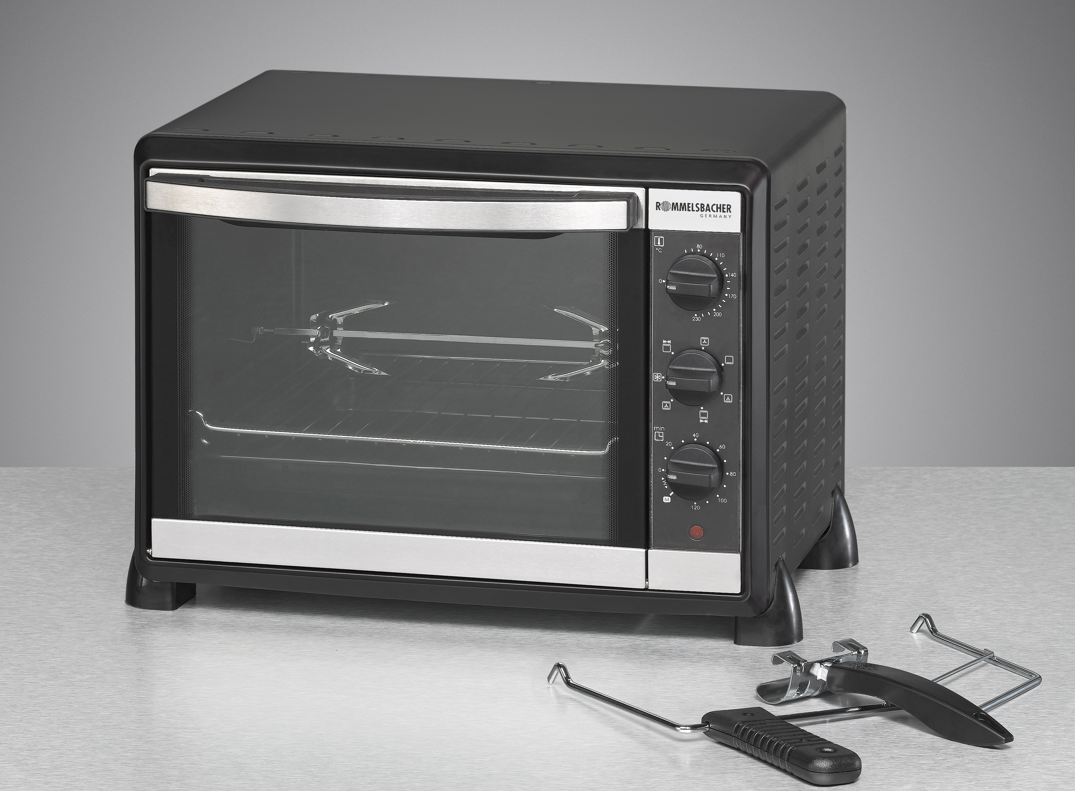 Schwarzer Elektrobackofen auf einem Tisch, mit Glastür und Drehspießaufsatz.