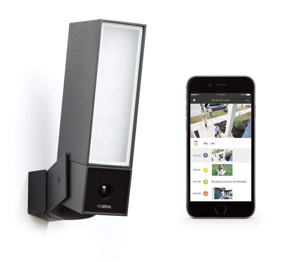 Een zwarte Netatmo beveiligingscamera en een smartphone met een live videostream van een huis.
