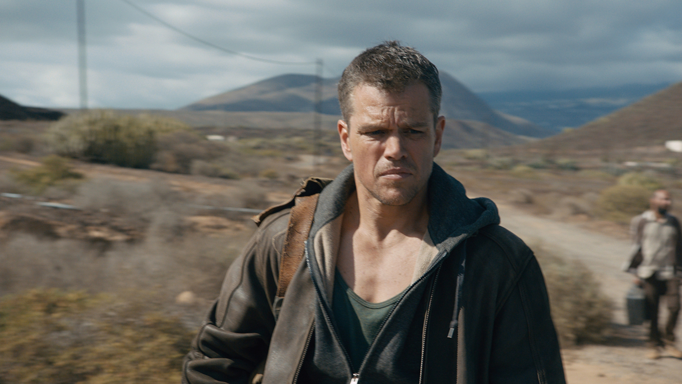 Matt Damon kijkt de camera in. Hij draagt een jas en een hoodie, met bergen op de achtergrond.