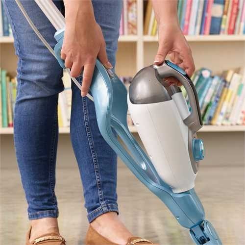 Person holding a blue and white steam mop. A bookshelf is in the background.