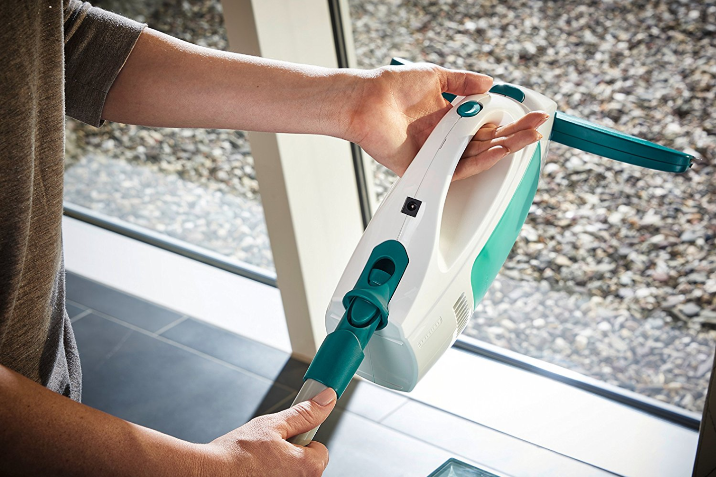 Persoon die een raamreinigingsapparaat vasthoudt met een witte behuizing en een turquoise handvat.