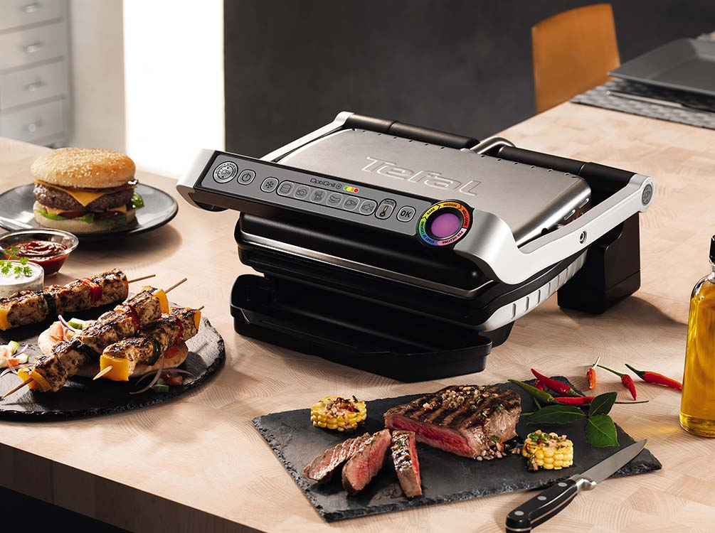 Tefal grill met eten. Biefstuk, spiesjes en burgers op tafel. Achtergrond is onscherp.