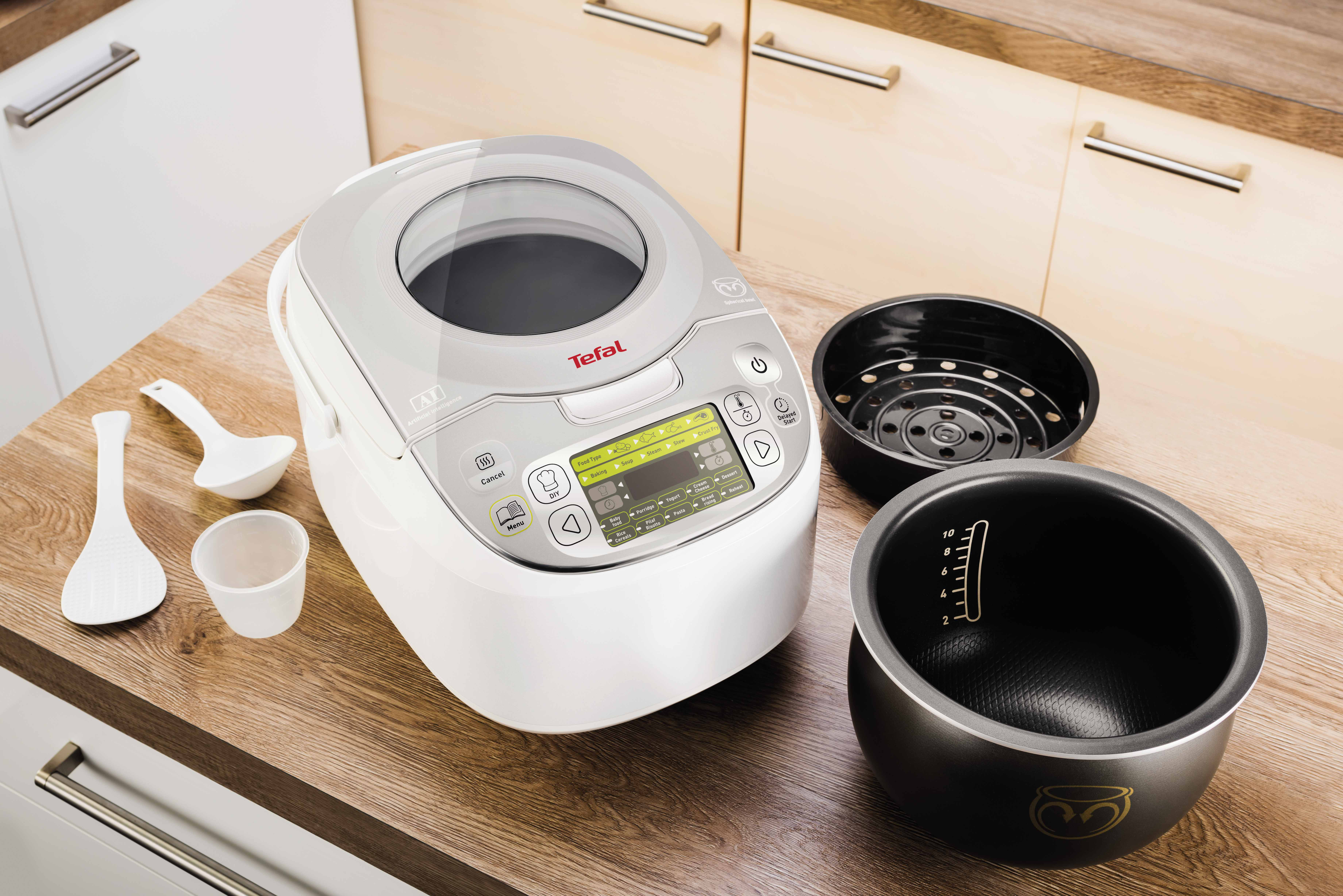Witte en grijze Tefal rijstkoker met accessoires. De koker staat op een houten oppervlak.