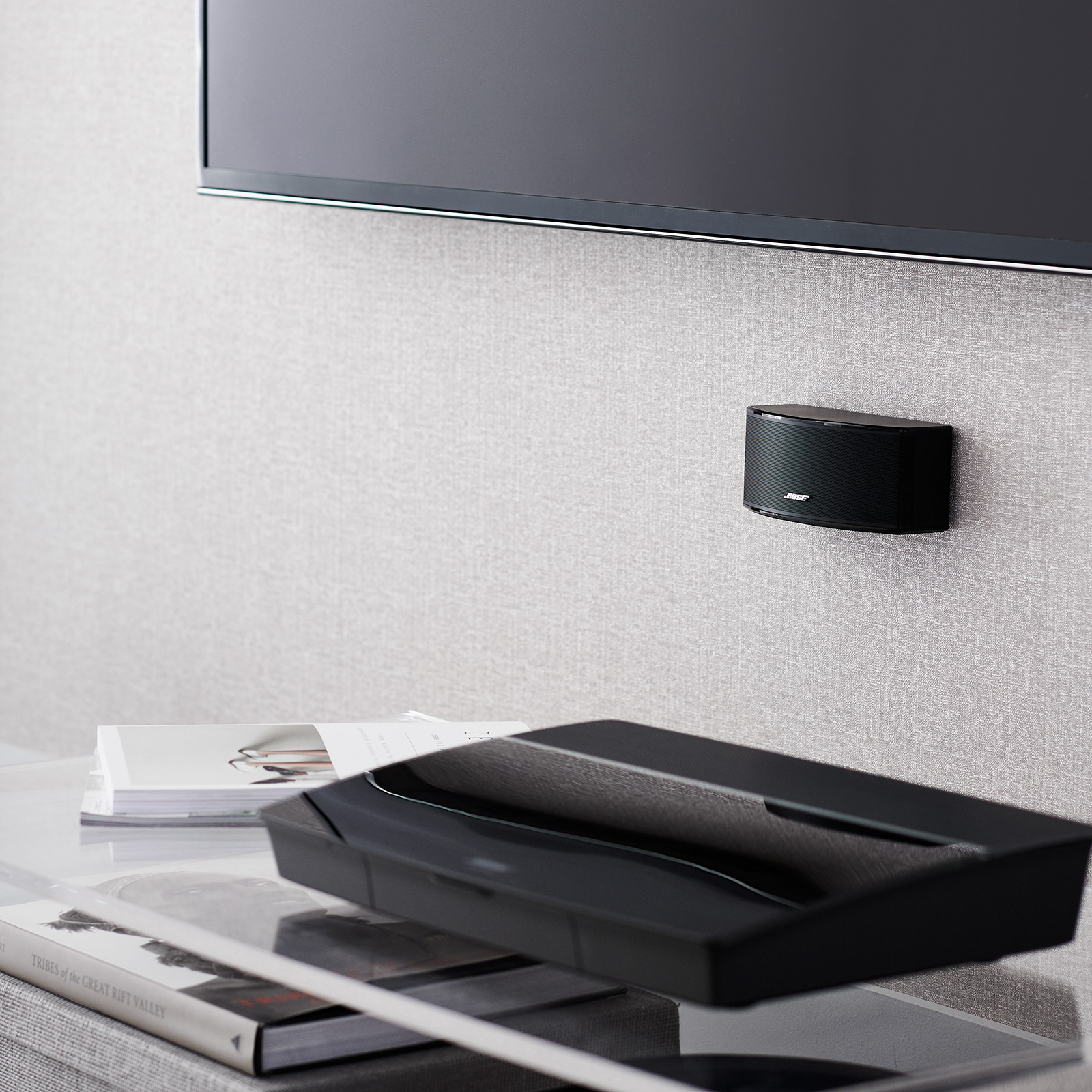 Schwarze Soundbar an einer grauen Wand montiert. Ein Fernseher ist darüber, ein schwarzer Lautsprecher.
