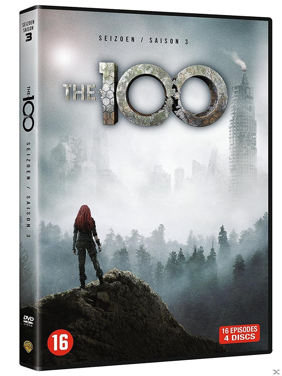 A woman with red hair stands on a rock, a ruined city in the fog.