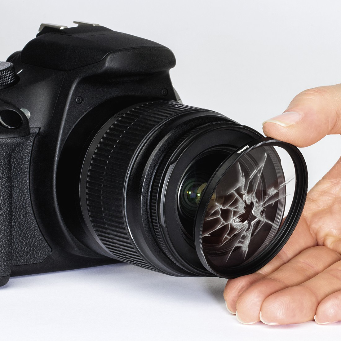 Eine DSLR-Kamera mit einem zerbrochenen Objektivfilter. Eine Hand hält den Filter.
