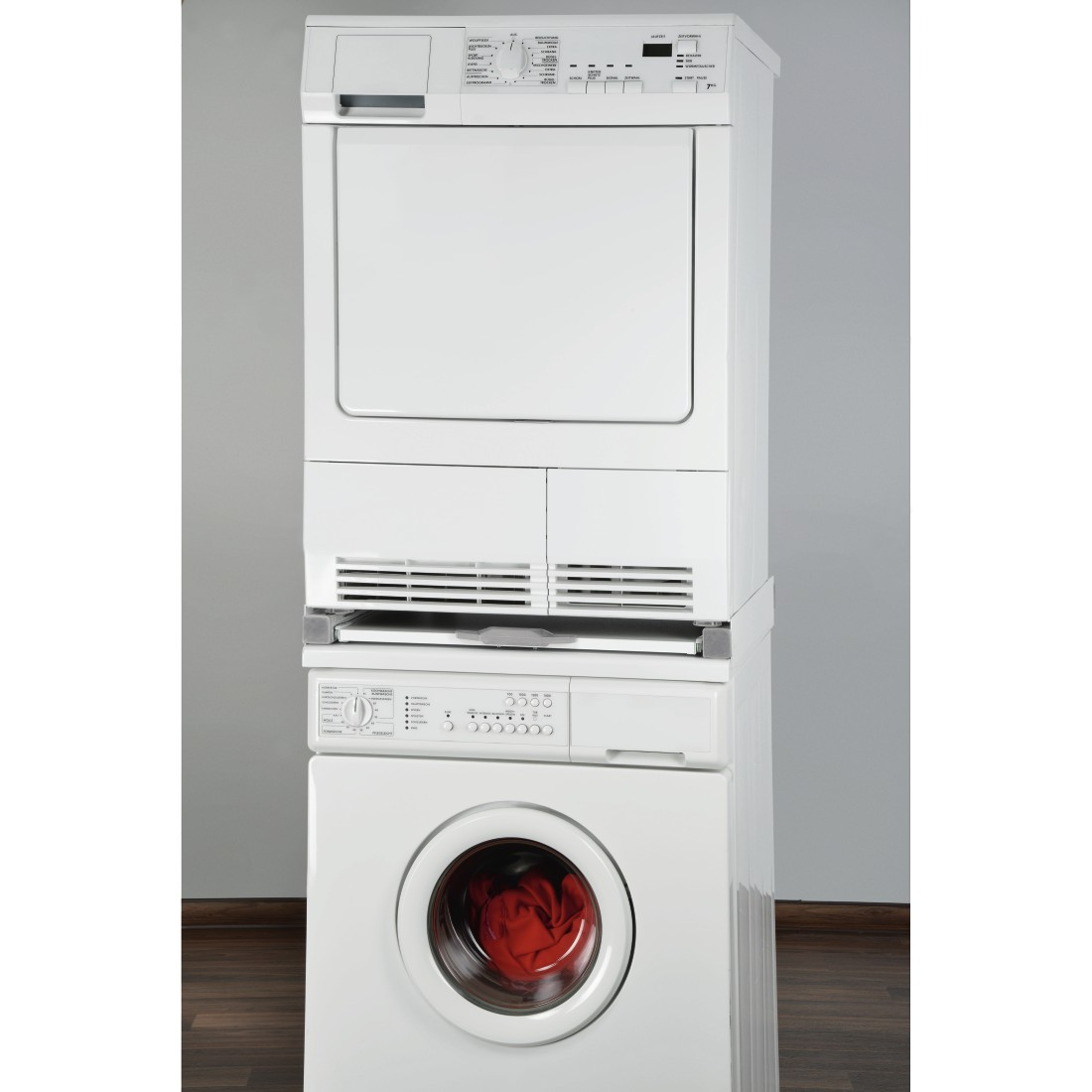Stacked white washing machine and dryer. Red laundry visible inside the washing machine drum.