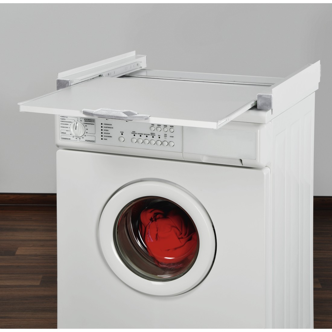 White washing machine with a raised, open top shelf. A red item is in the glass door.