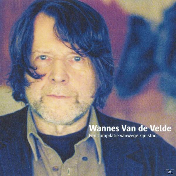 Een man met kort blauw haar en een baard kijkt naar voren. Er is tekst aanwezig. De achtergrond is wazig.