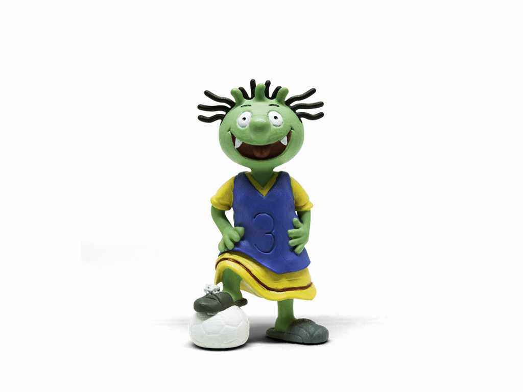 Eine grüne Zeichentrickfigur in einem blauen Trikot und gelben Shorts, die auf einem Fußball steht.