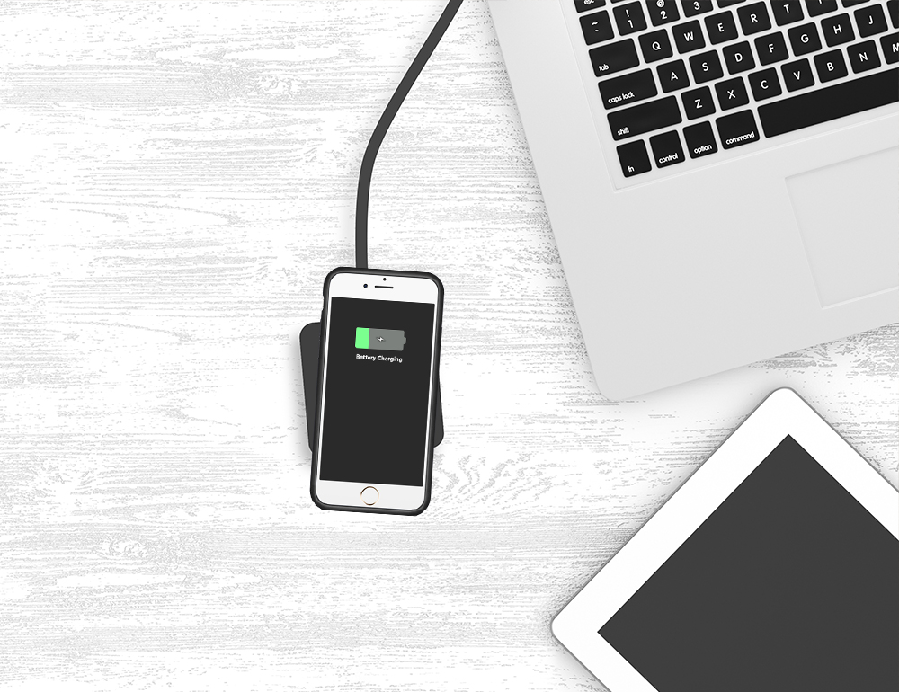 Ahşap bir masada bir dizüstü bilgisayar ve bir tabletin yanında, bir ped üzerinde kablosuz olarak şarj olan bir akıllı telefon.