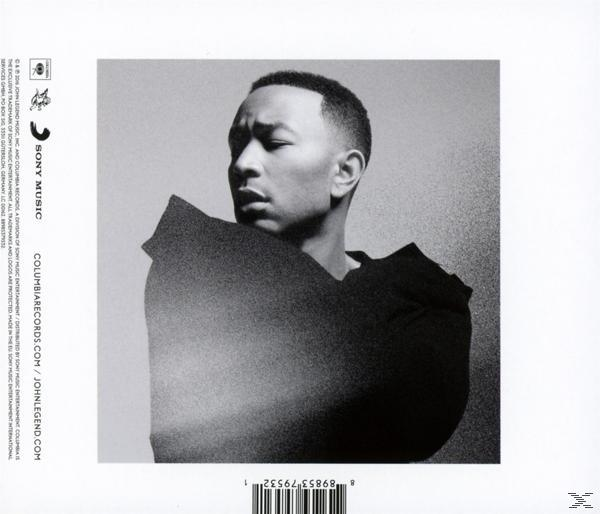 Ein Graustufenbild von John Legend. Er schaut nach links. Er trägt ein schwarzes Hemd mit verschwommenem schwarzem Hintergrund.