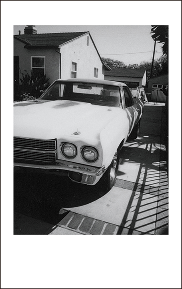 Black and white photo of a classic car parked in a driveway, in front of a house.