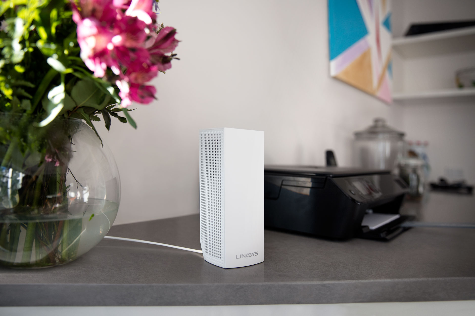 White router. Flowers in glass vase on the left, printer on the right. Gray countertop.