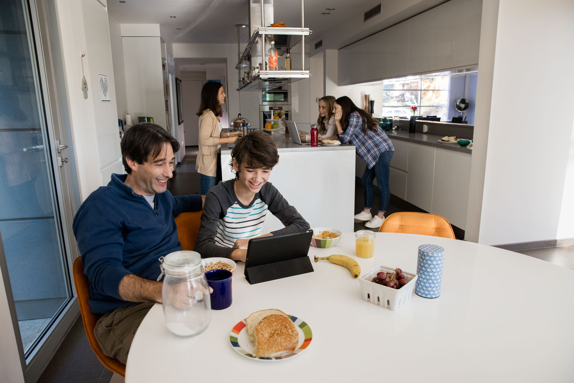 Family in a modern kitchen, a father and son at the table, others in the background.