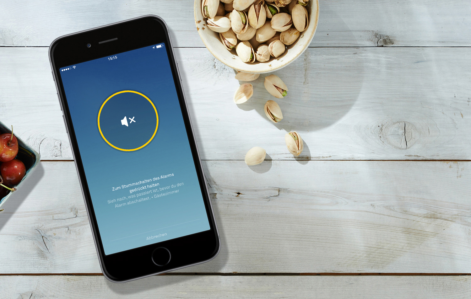 Smartphone auf Holztisch zeigt Alarm-Mute-App, daneben Pistazien und Kirschen.