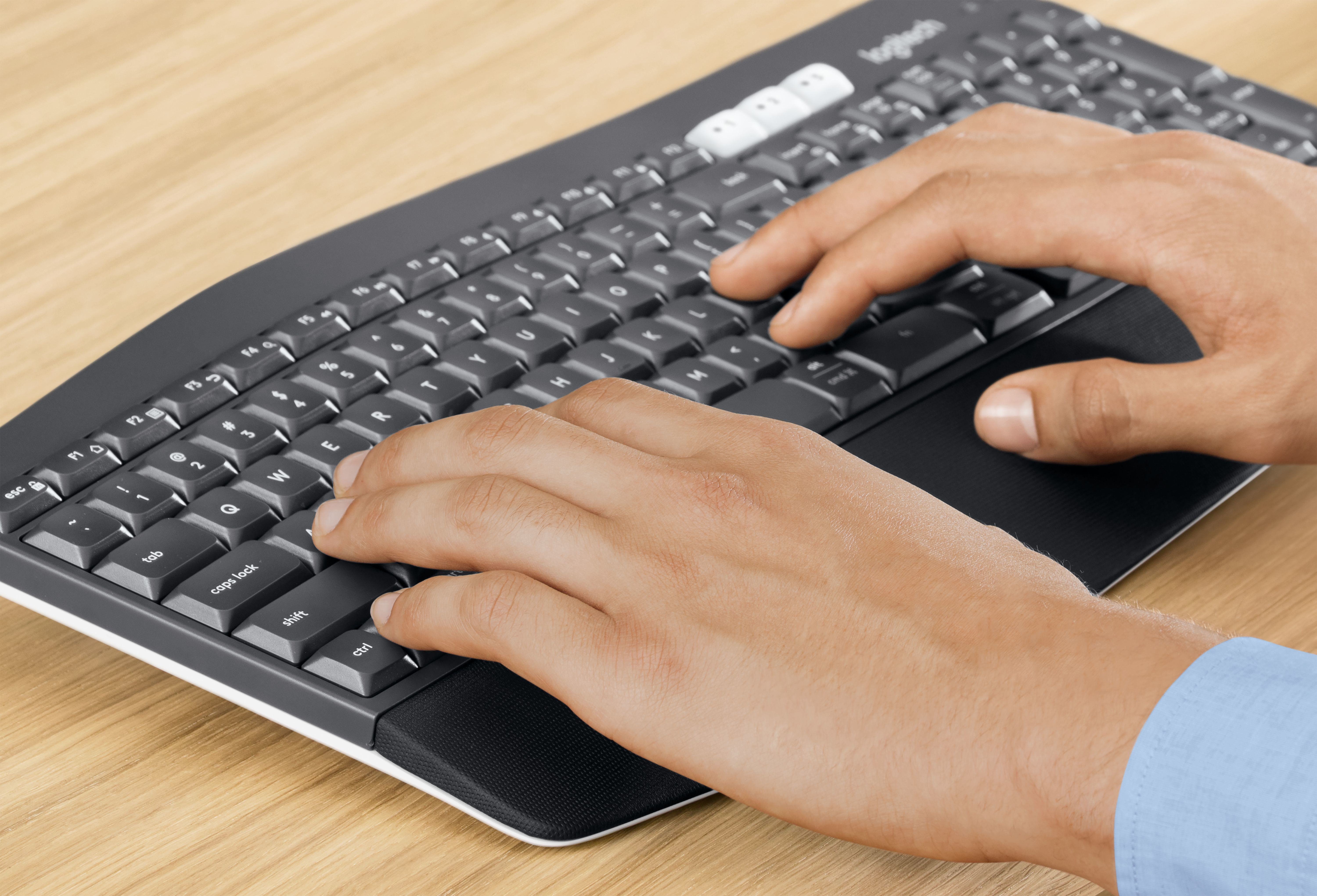 Hände tippen auf einer dunkelgrauen, ergonomischen Tastatur. Holzschreibtisch. Fokus auf Hände und Tastatur.