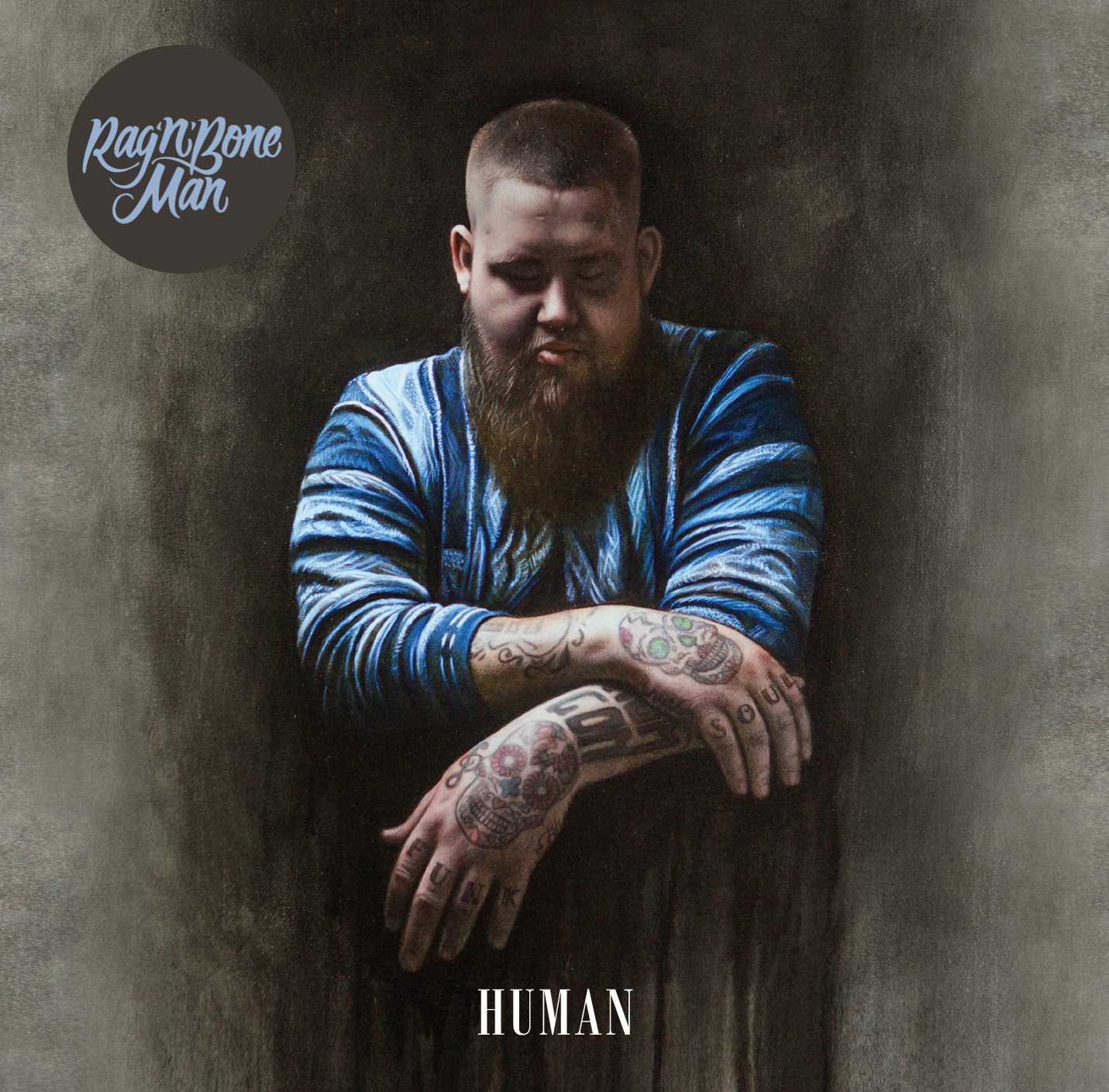 Rag'n'Bone Man mit Tätowierungen auf den Armen. Er trägt ein blau-weiß gestreiftes Hemd.