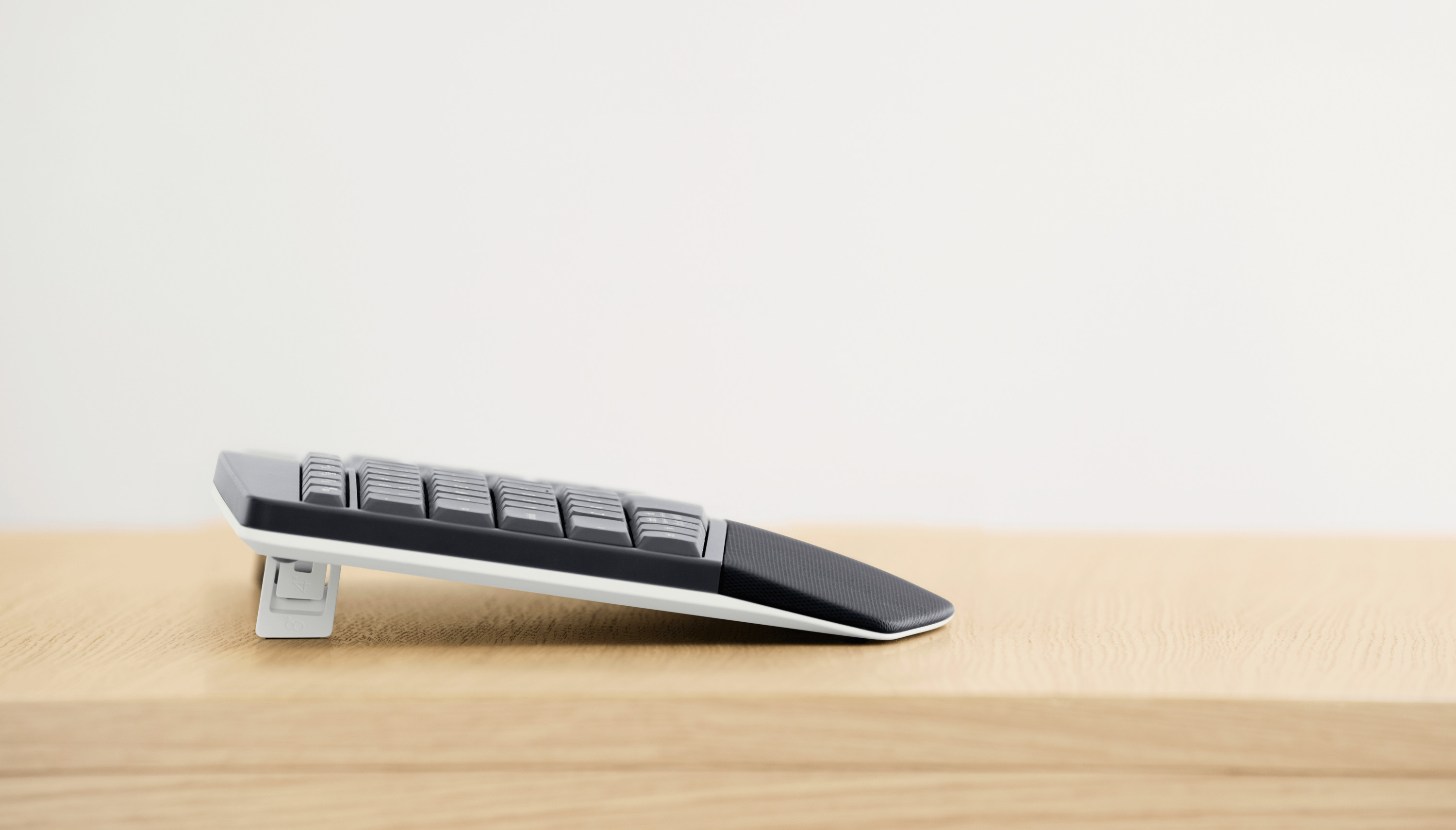 Side view of a black and gray keyboard on a wooden surface, against a white wall.
