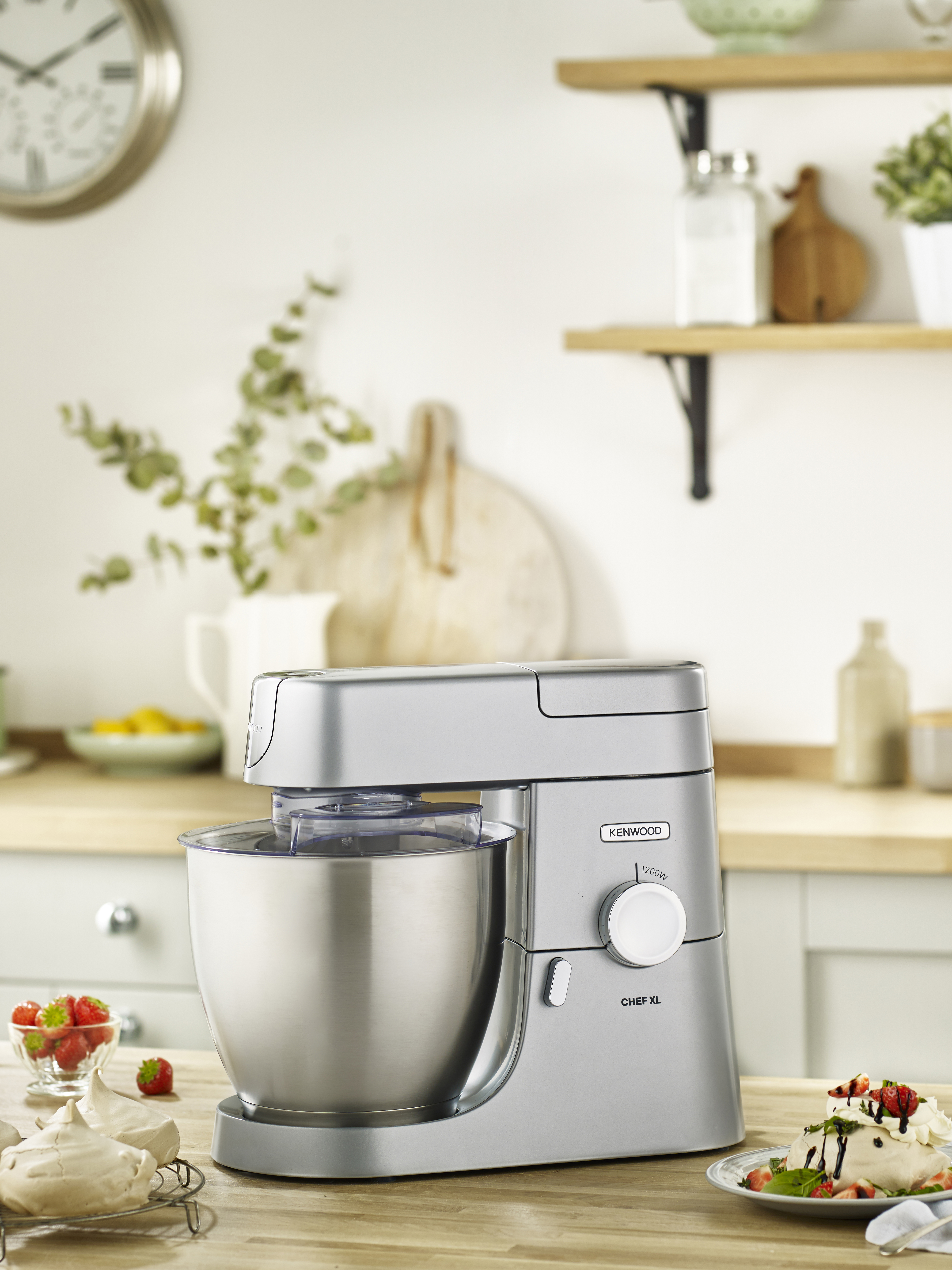 Silberner Kenwood Chef XL Küchenmixer auf Holz. Zutaten und Dekoration im Hintergrund.