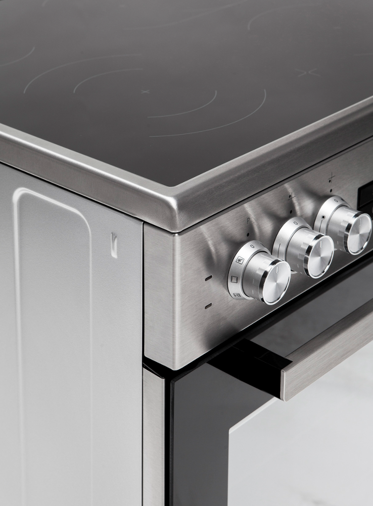 Close-up van een roestvrijstalen elektrisch fornuis. Knoppen en een zwarte glazen kookplaat zijn zichtbaar. De ovendeurgreep is ook zichtbaar.