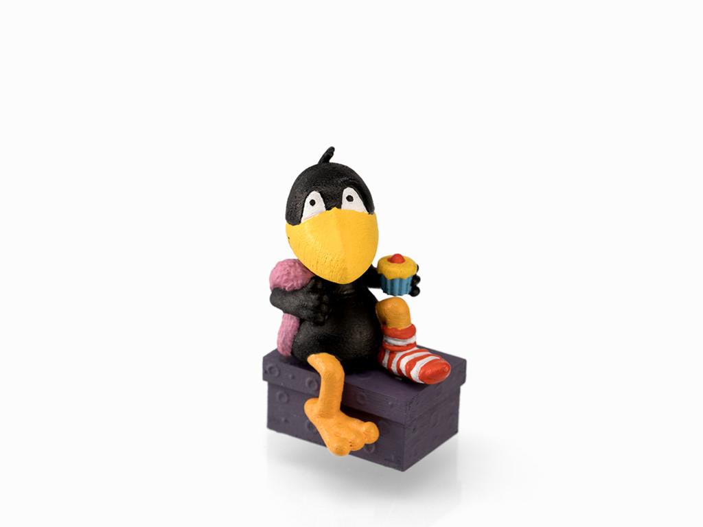 Eine Cartoon-Krähenfigur sitzt auf einer lila Kiste, hält einen Cupcake und eine Socke, auf weißem Hintergrund.