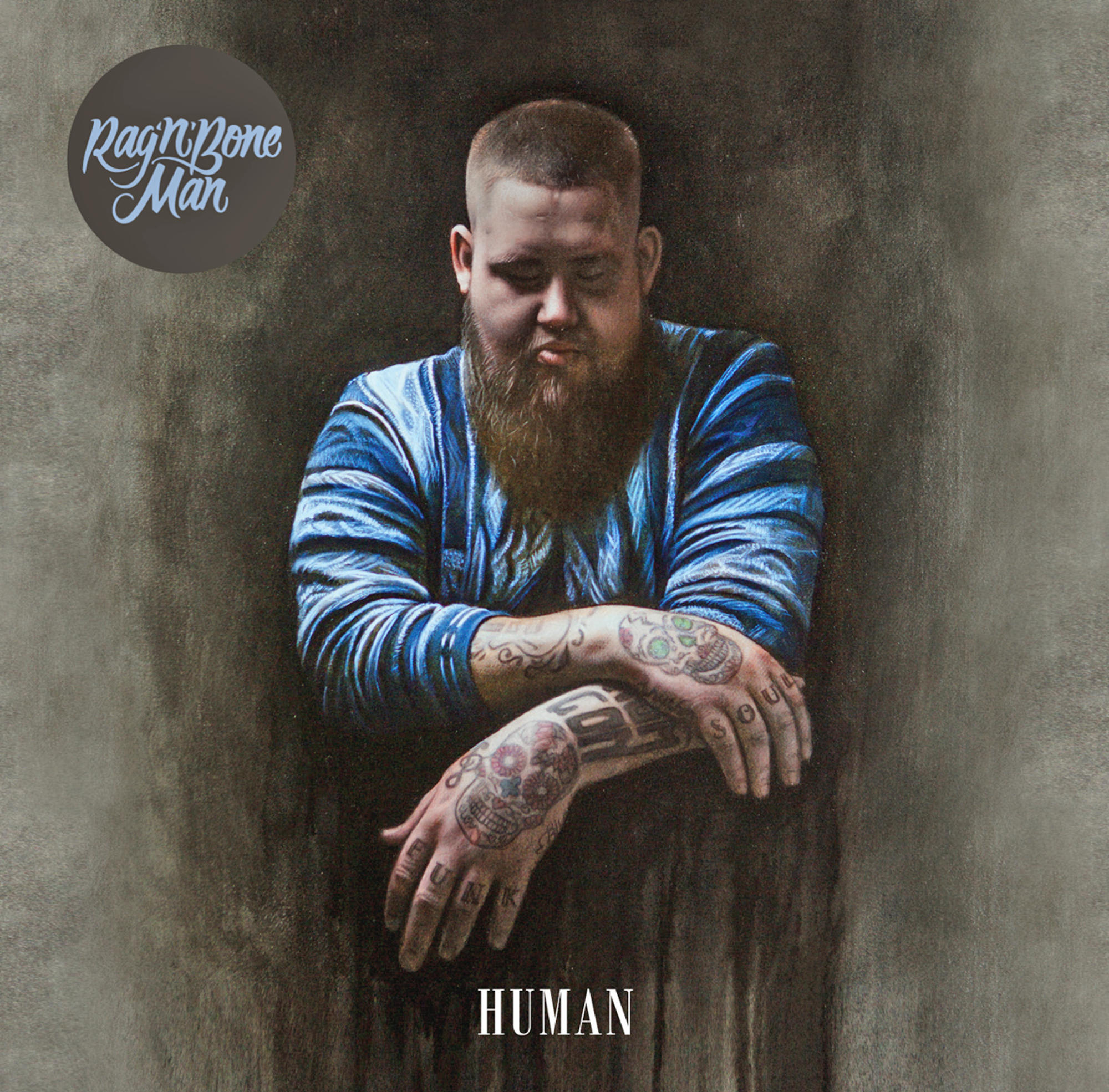 Rag'n'Bone Man mit Tätowierungen. Er trägt ein blau gestreiftes Hemd und hat einen Bart.