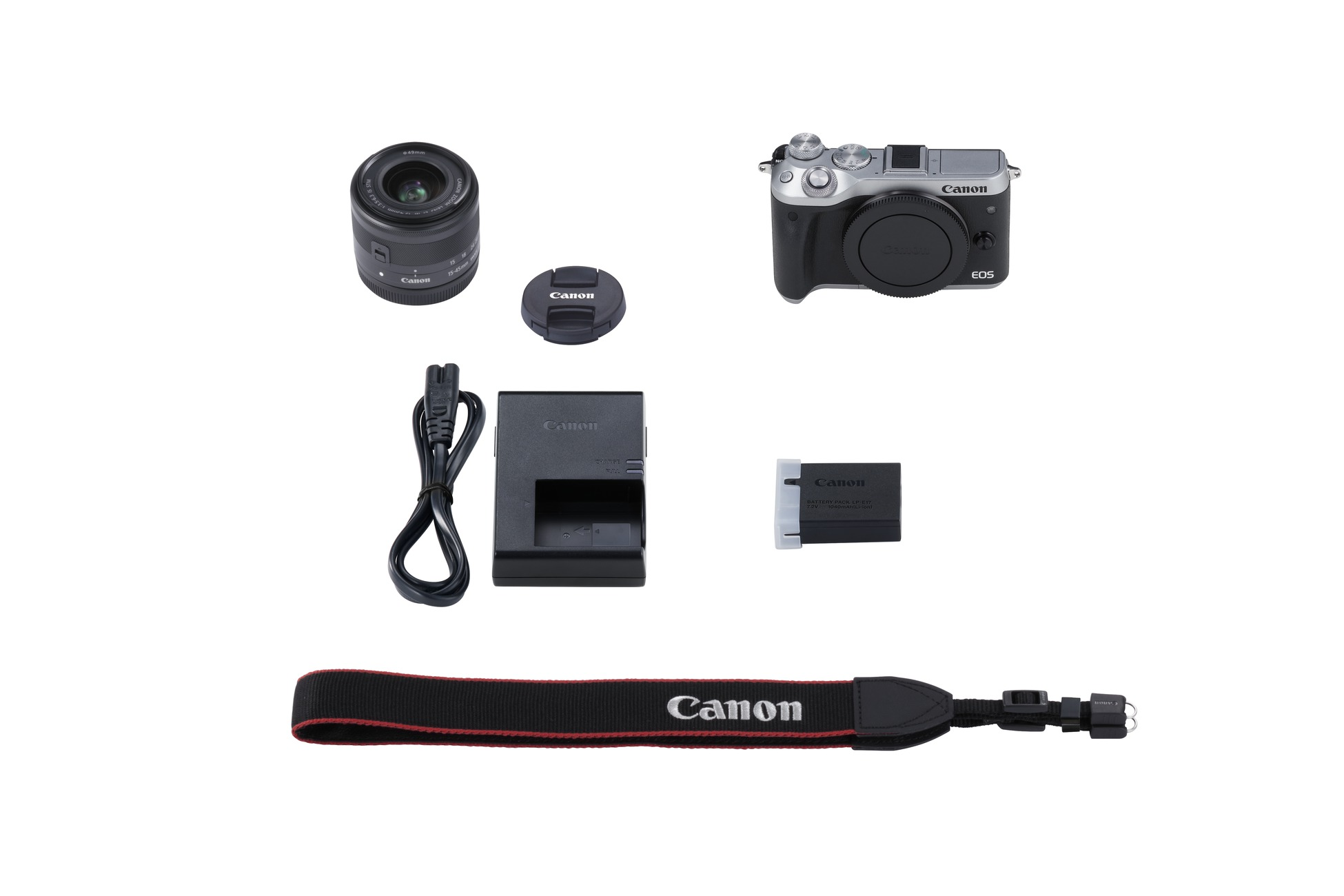 Camerakit met camerabody, lens, batterij, oplader en riem, alles op witte achtergrond.