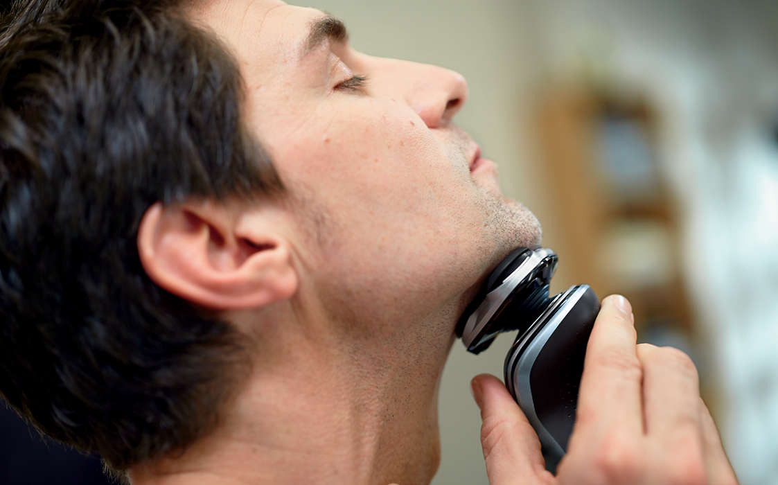 A man shaving with an electric razor, close-up on his face.