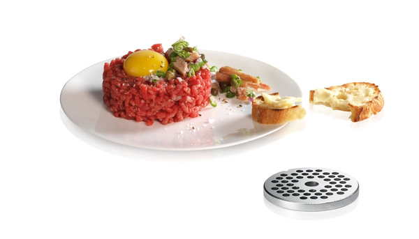 Rohes Fleisch-Tartar mit Eigelb, Kapern, Brot und einem Metallschleifer auf einem weißen Teller.