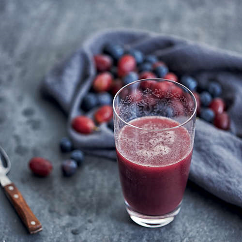 Glass of red juice with berries and a cloth in the background. A spoon is on the left.