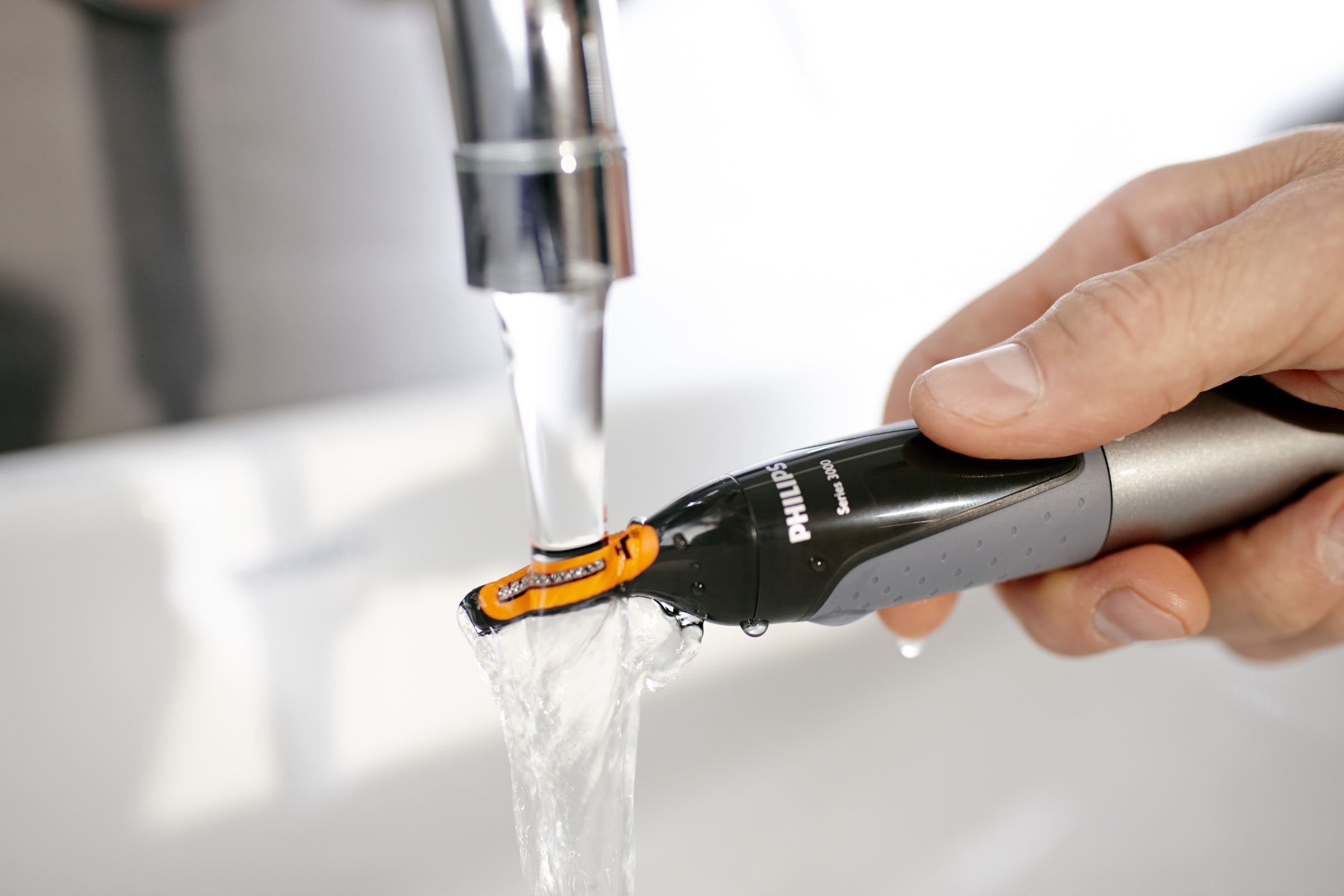 Ein Philips Nasenhaartrimmer unter fließendem Wasser. Der Kopf ist orange.