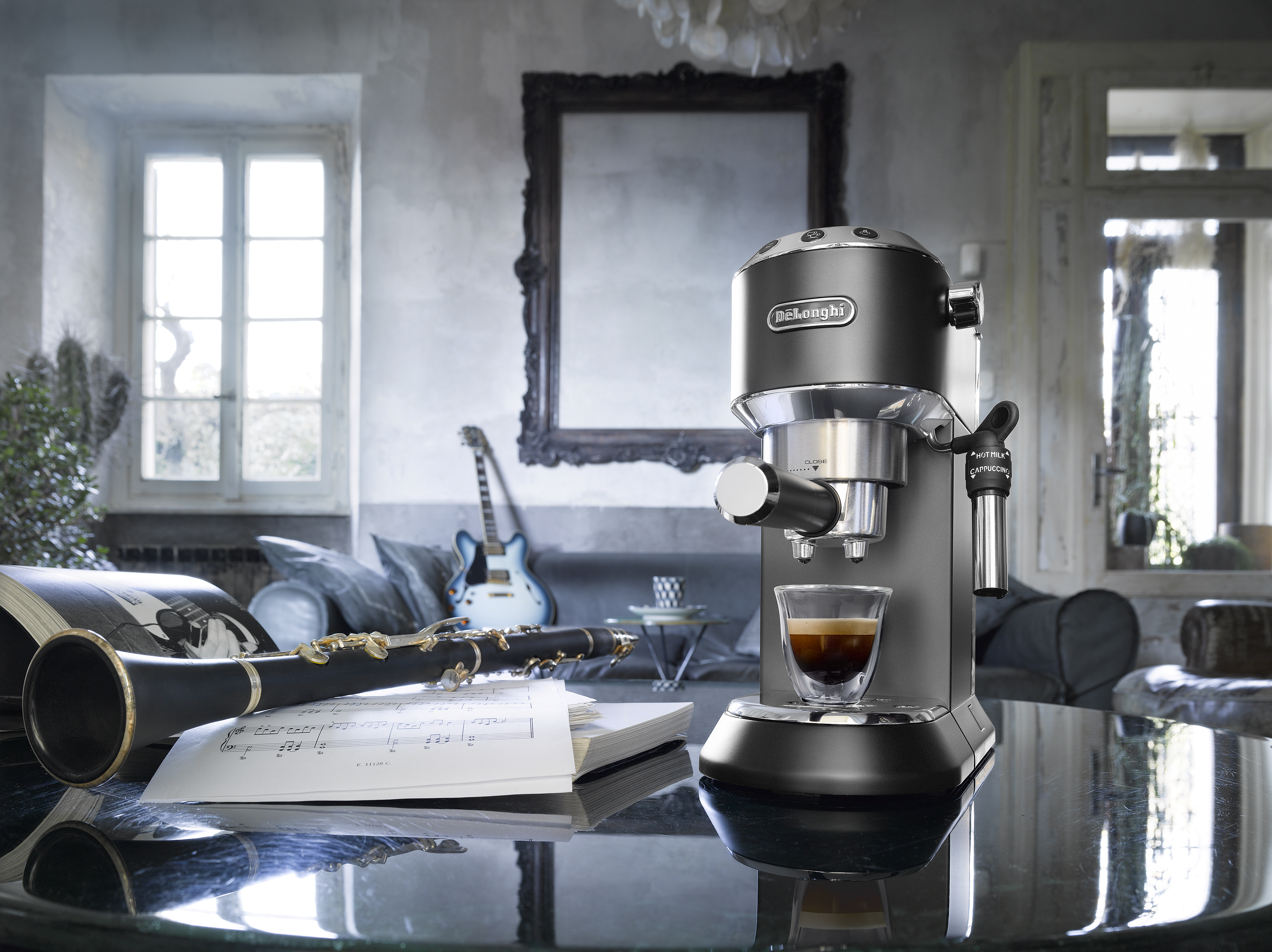 Espressomachine, klarinet en bladmuziek op een tafel, met een gitaar op de achtergrond.