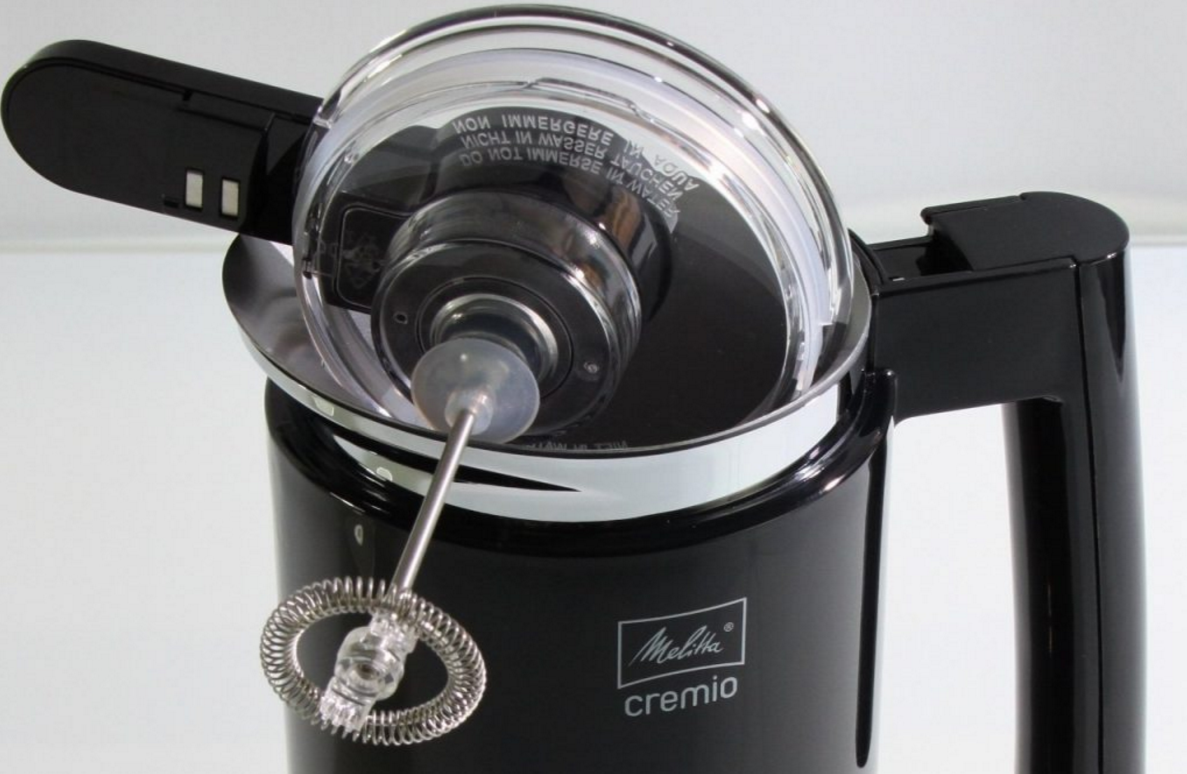 A black milk frother with a clear lid, with a metal whisk inside, close up on white.