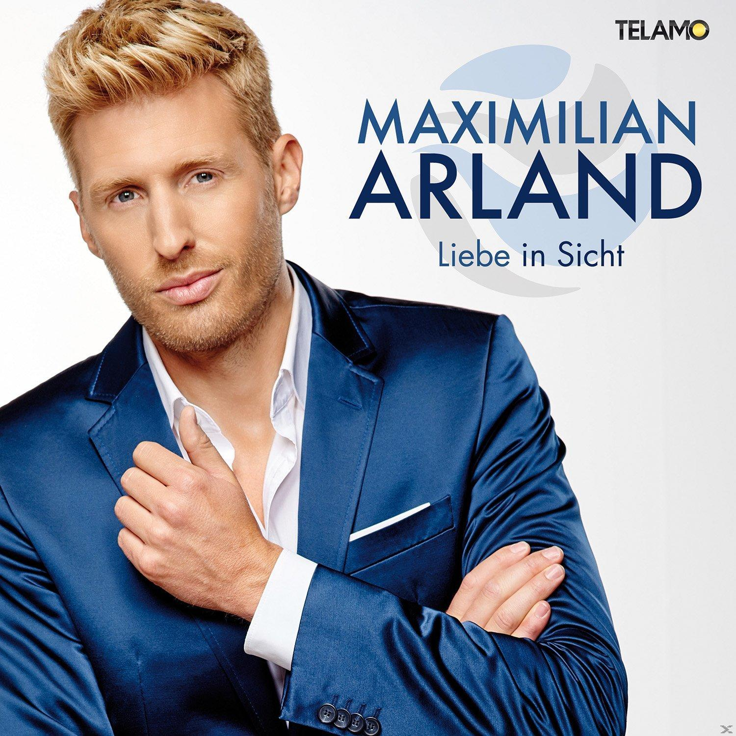 Mann in blauem Anzug. Blondes Haar und weißes Hemd. Der Text 'Maximilian Arland' steht oben.