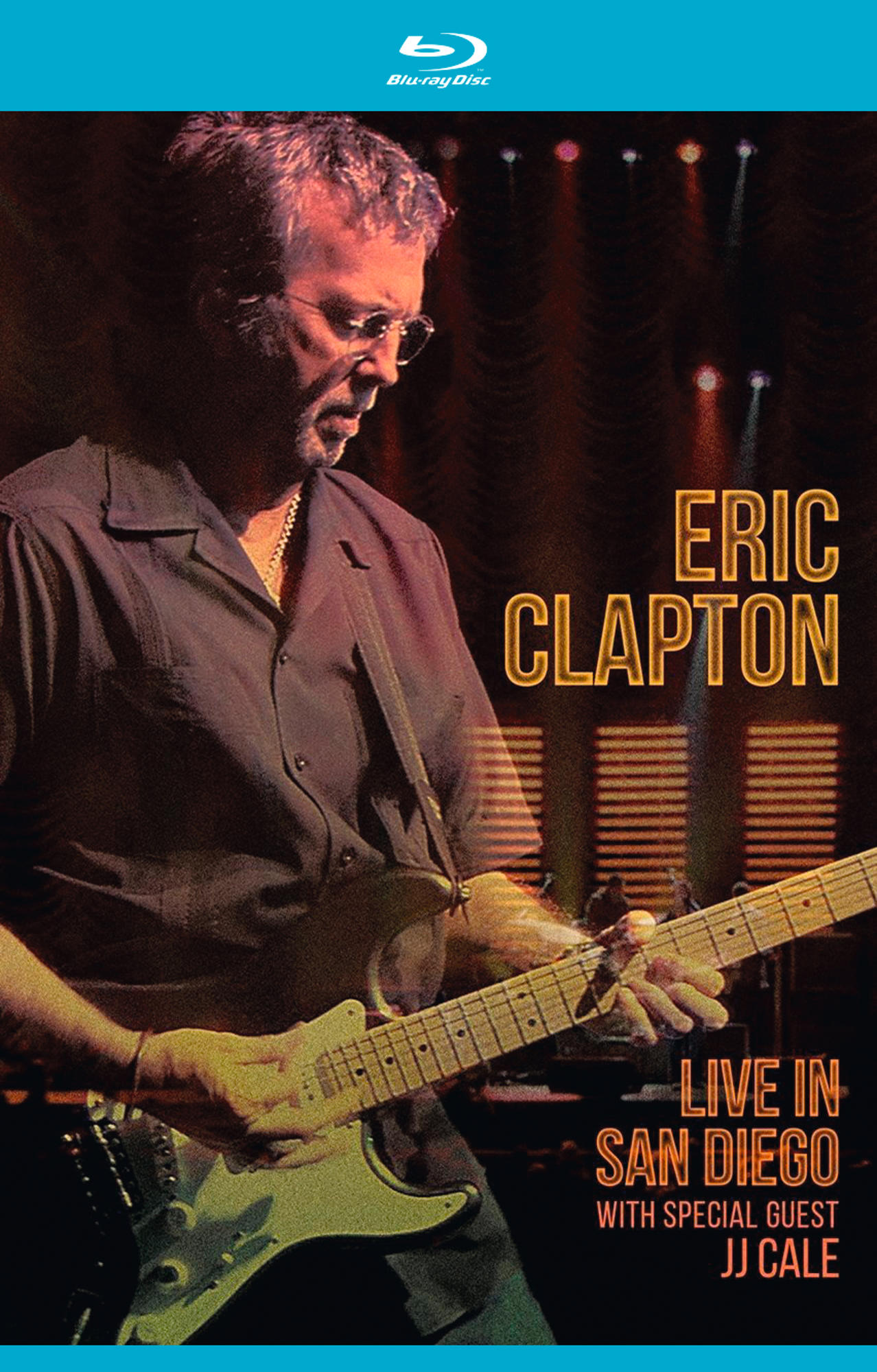 Eric Clapton auf der Bühne beim Gitarrespielen. Das Bild hat Konzertbeleuchtung, und er trägt eine Brille.