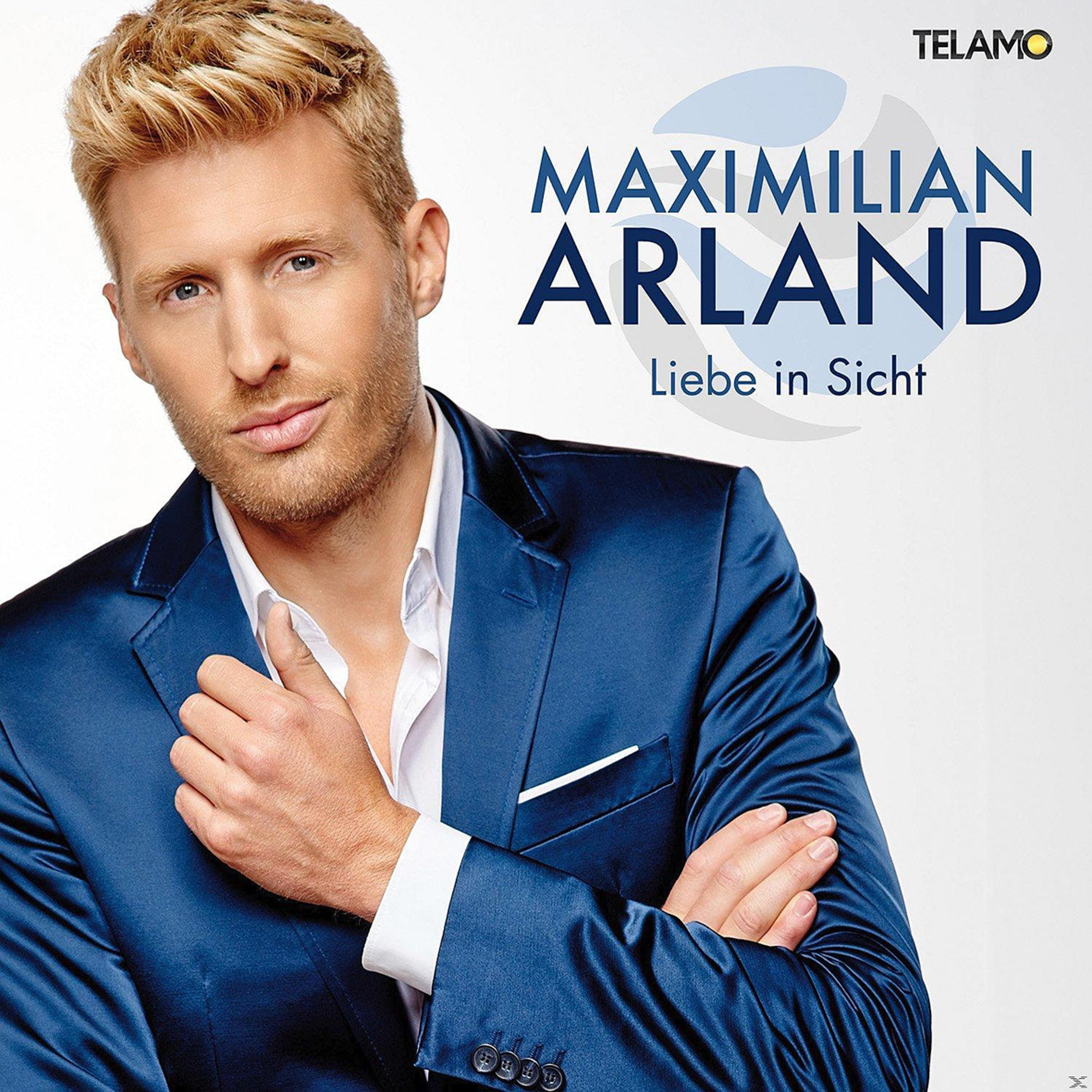 Maximilian Arland in blauem Anzug vor weißem Hintergrund. Titel 'Liebe in Sicht' sichtbar.