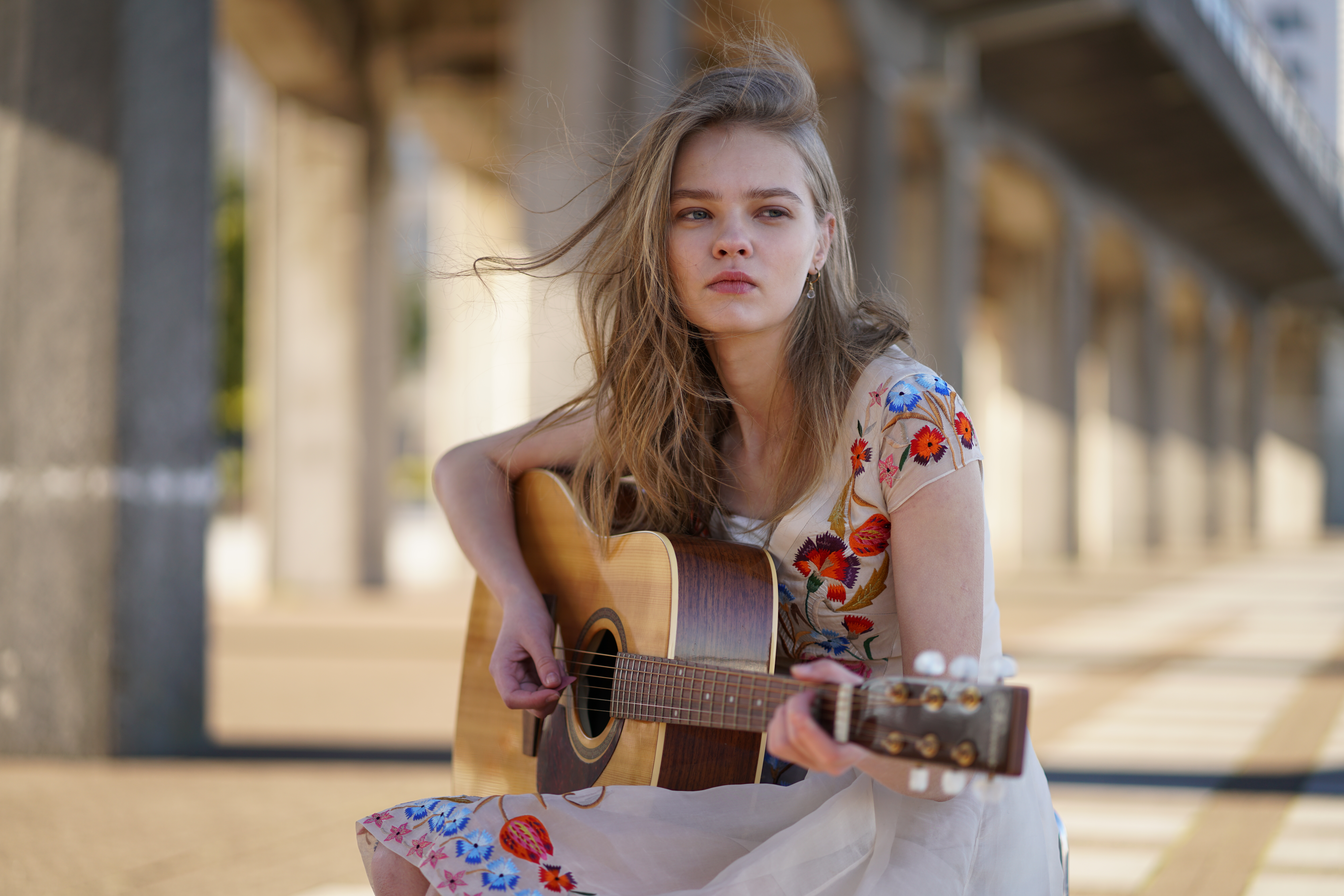Une femme en robe blanche avec une guitare, jouant sous un pont.