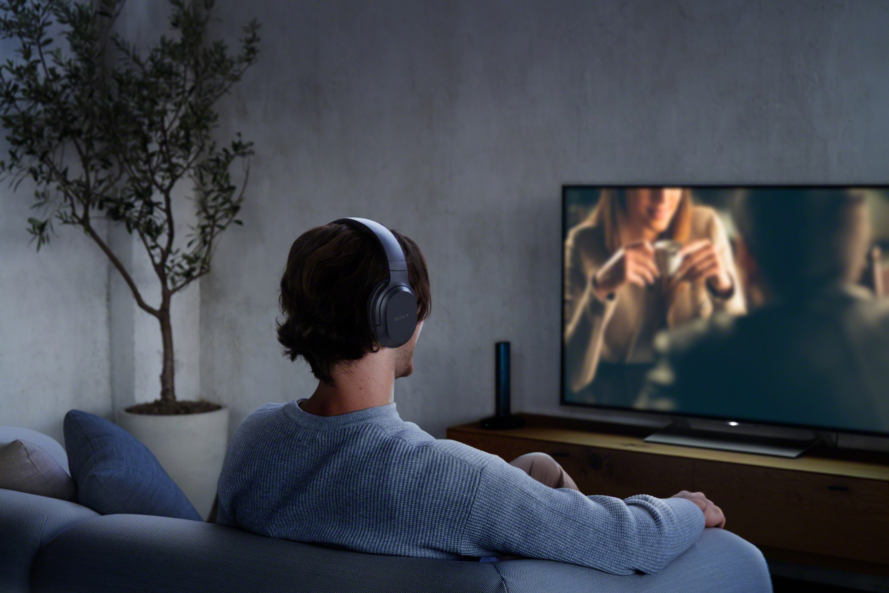 Un homme portant un casque regarde la télévision. Arrière-plan flou du salon.
