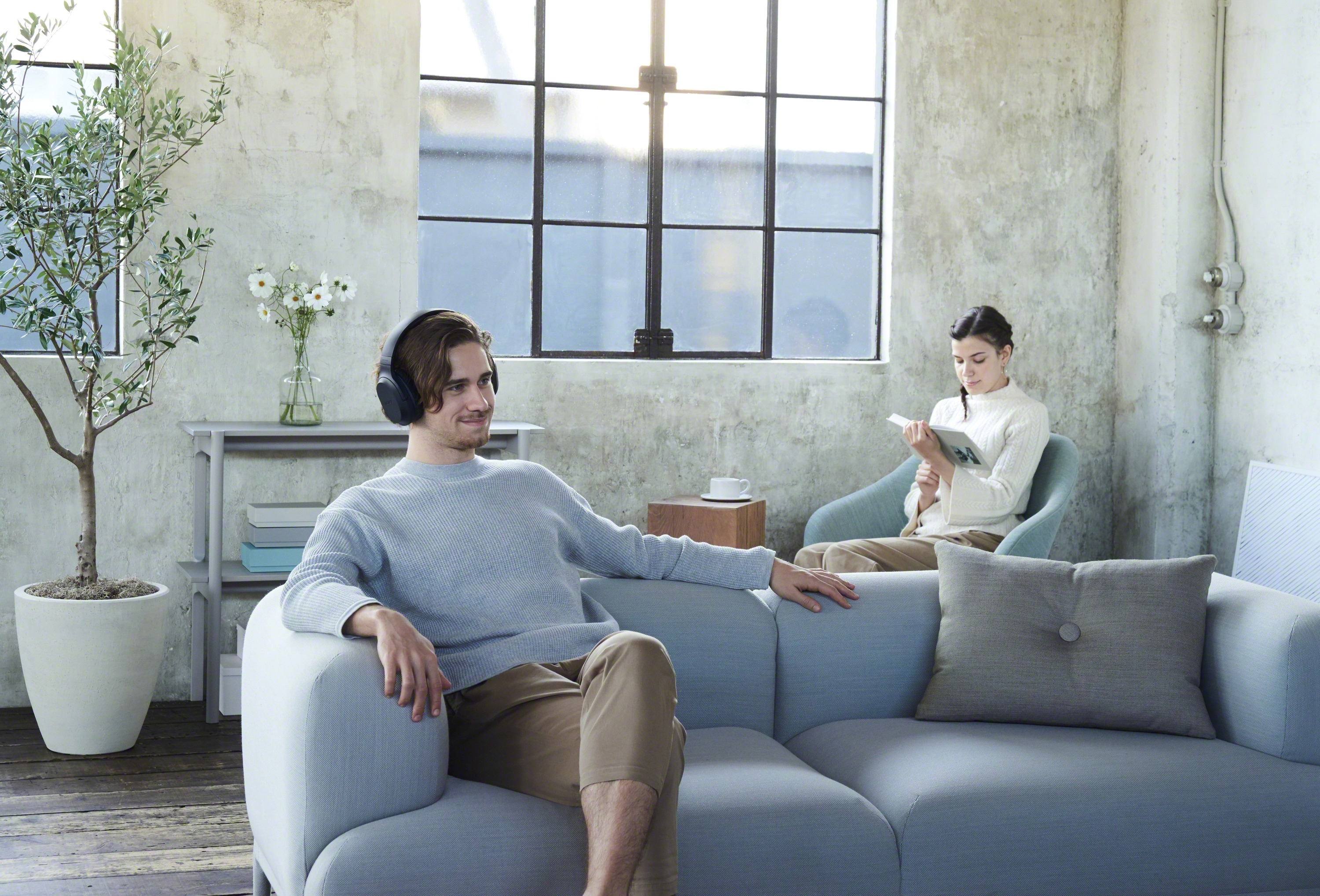 Scène de salon moderne avec un homme portant un casque, assis sur un canapé, et une femme lisant.
