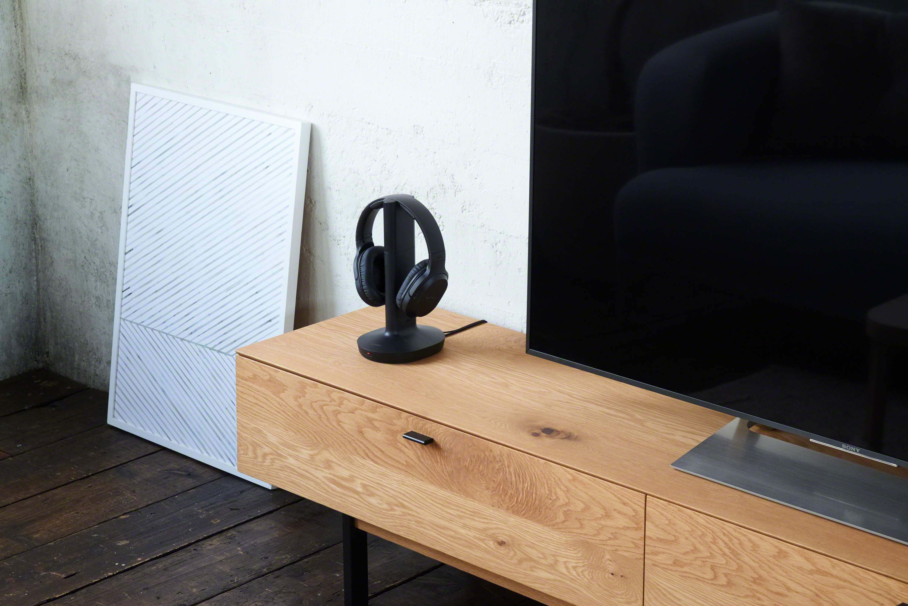 Un salon moderne avec une télévision, un meuble en bois, un casque sur un support et une œuvre d'art blanche.