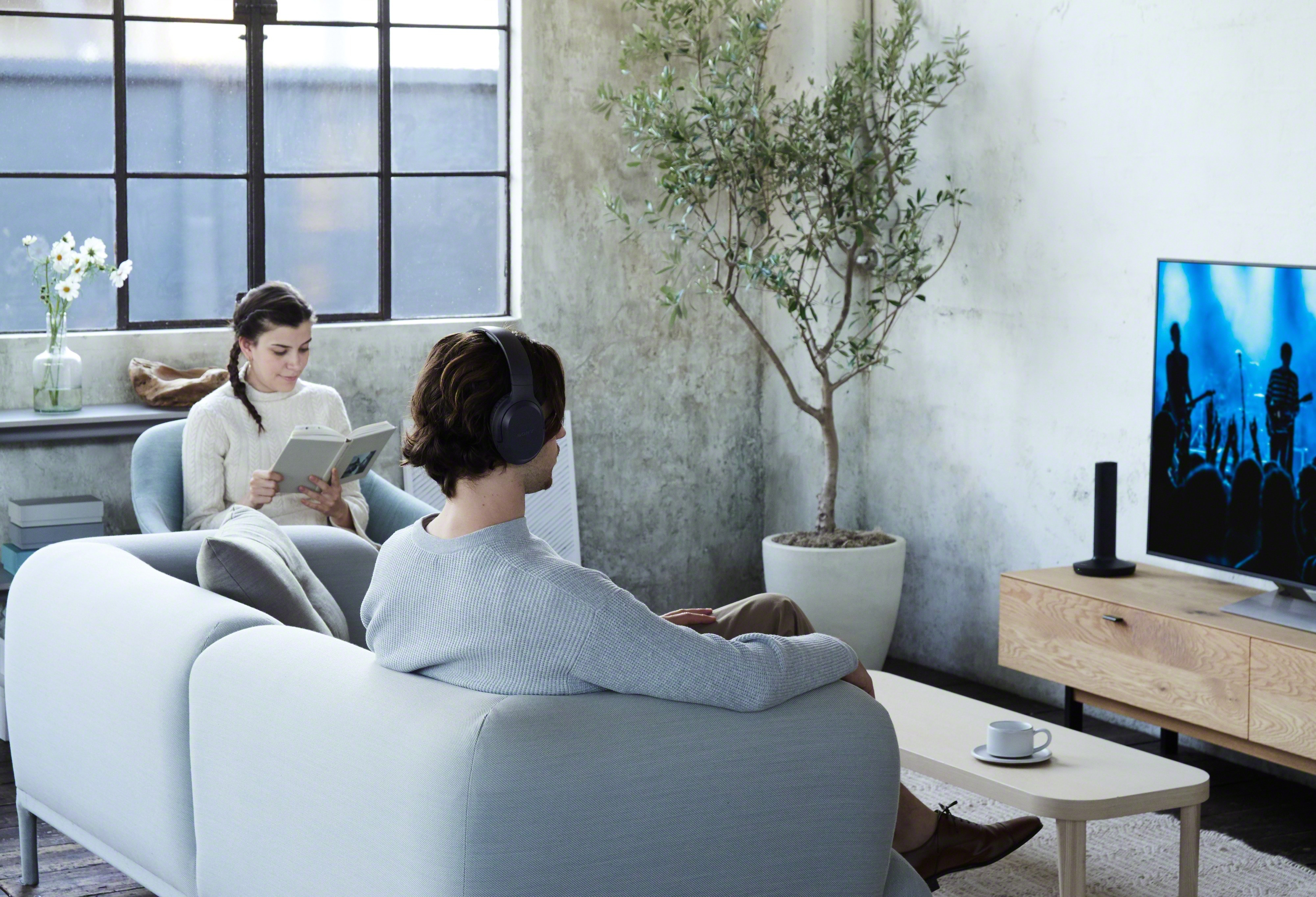 Deux personnes écoutant de la musique avec des écouteurs sur un canapé, près d'une TV.