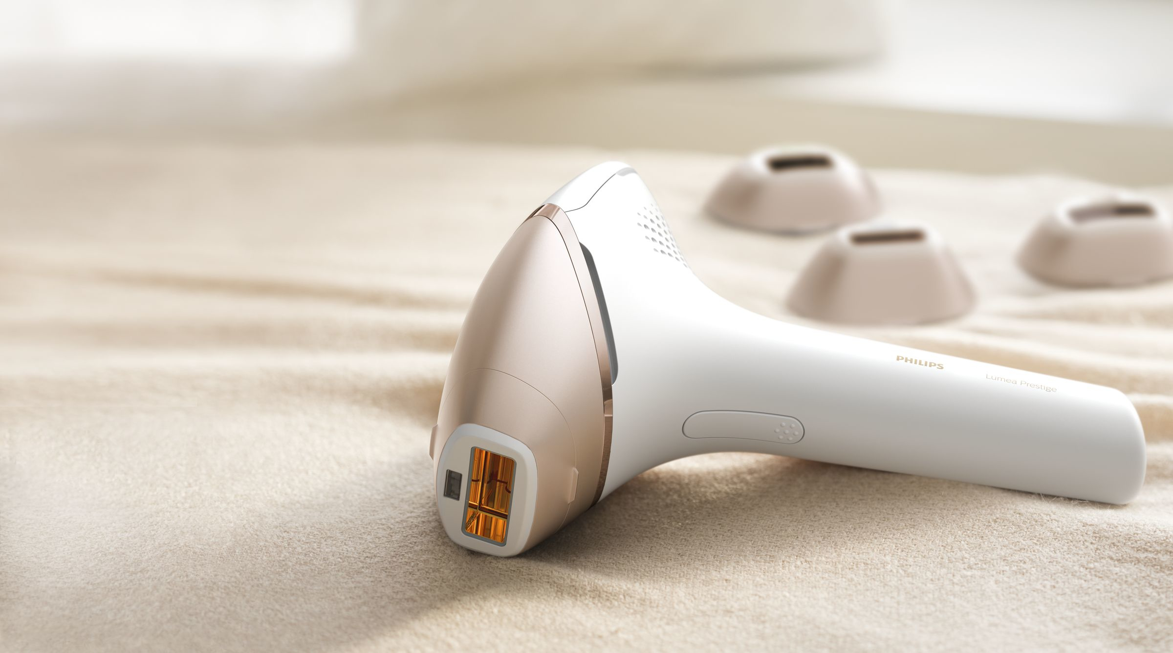 Ein weißes und goldenes Philips Lumea Prestige Haarentfernungsgerät auf einer beigen Oberfläche mit drei Köpfen.
