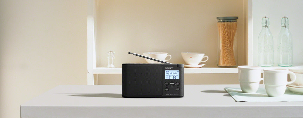 Une radio SONY noire sur une surface blanche, près d'une fenêtre, avec des tasses.