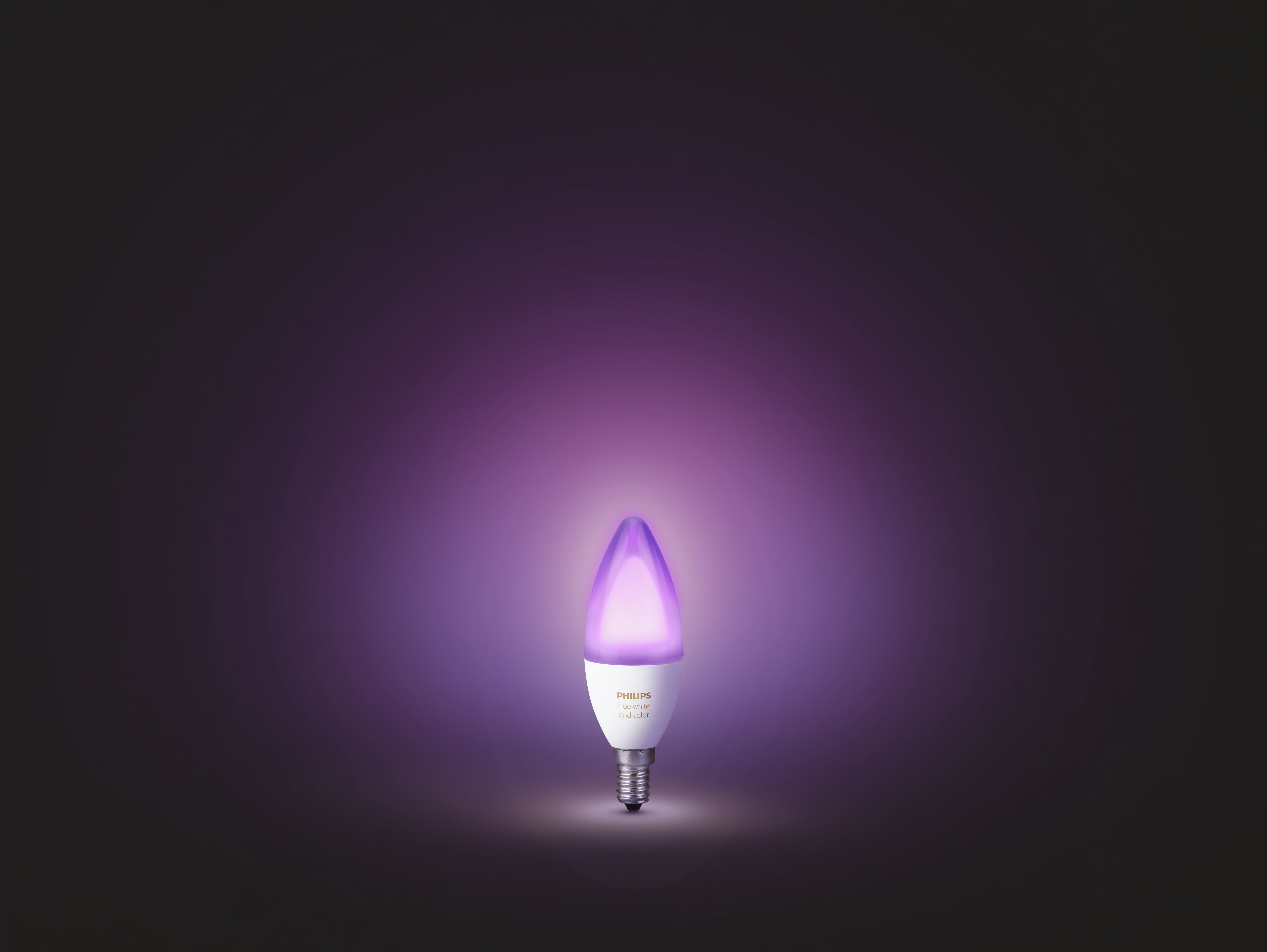 Eine violett leuchtende Glühbirne mit Kerzenfuß vor einem violett-schwarzen Hintergrund.