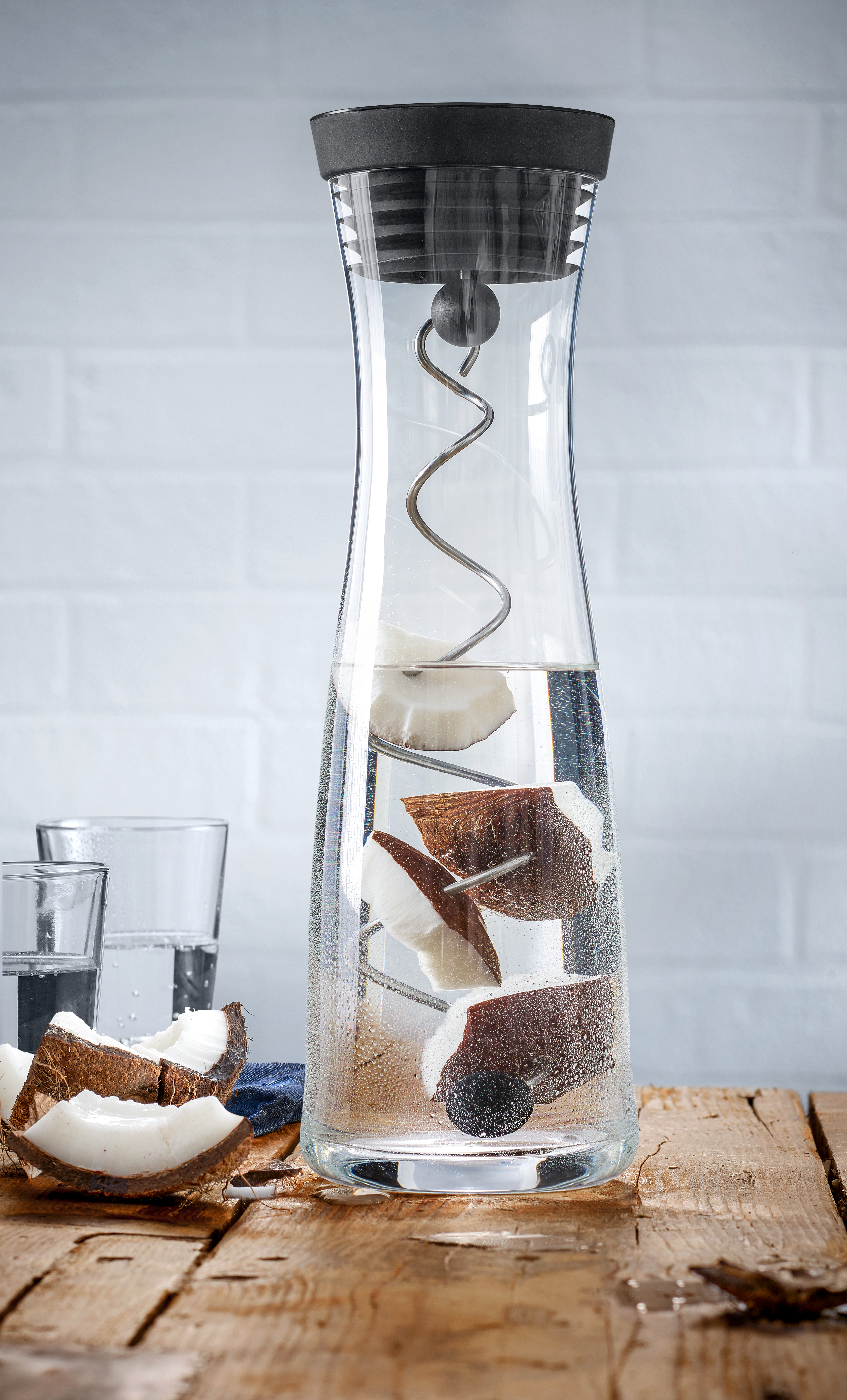 Eine klare Wasserkaraffe mit Kokosnuss-Scheiben und ein Holztisch.