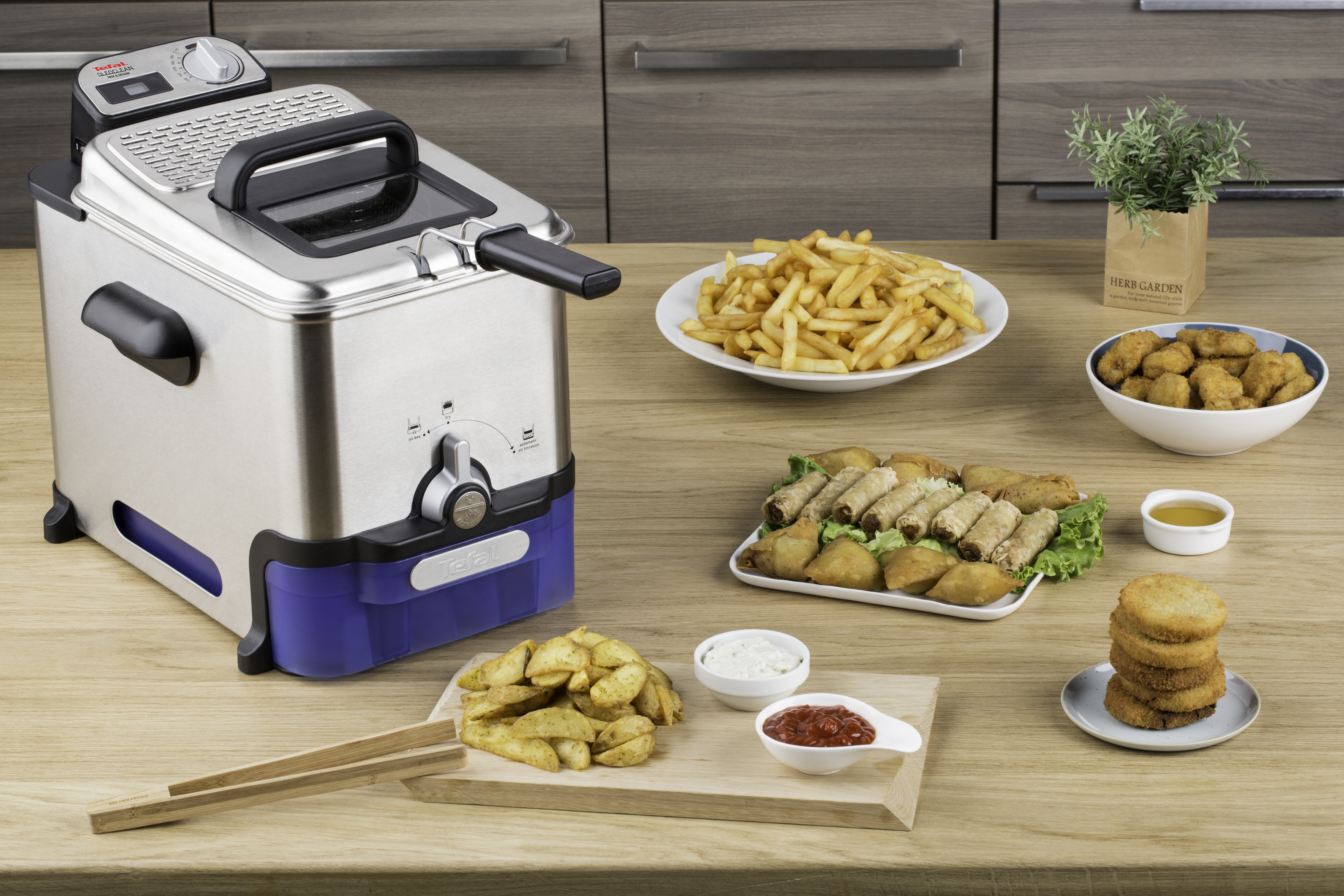 Een roestvrijstalen friteuse met diverse gefrituurde gerechten op een houten tafel.