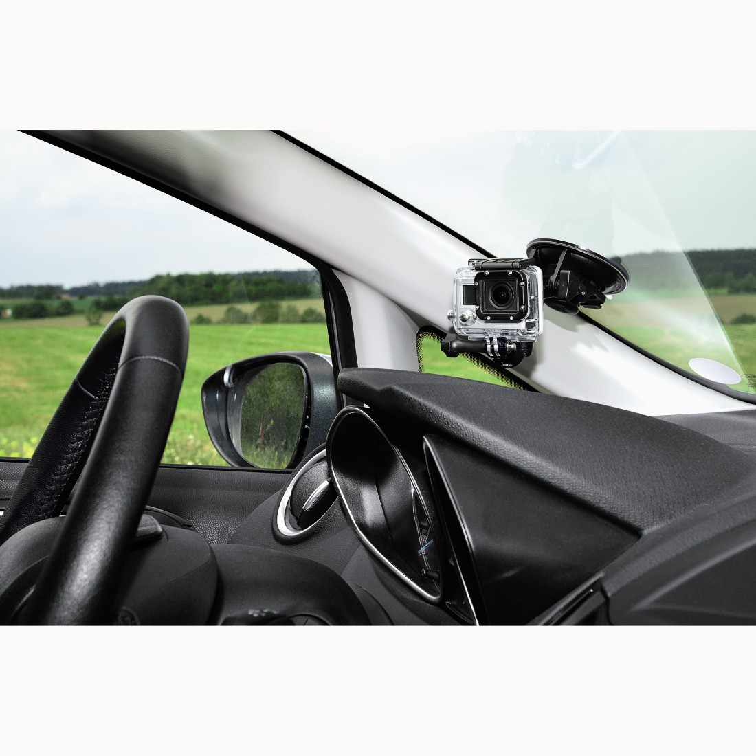 A GoPro camera mounted inside a car, with a green field in the background.